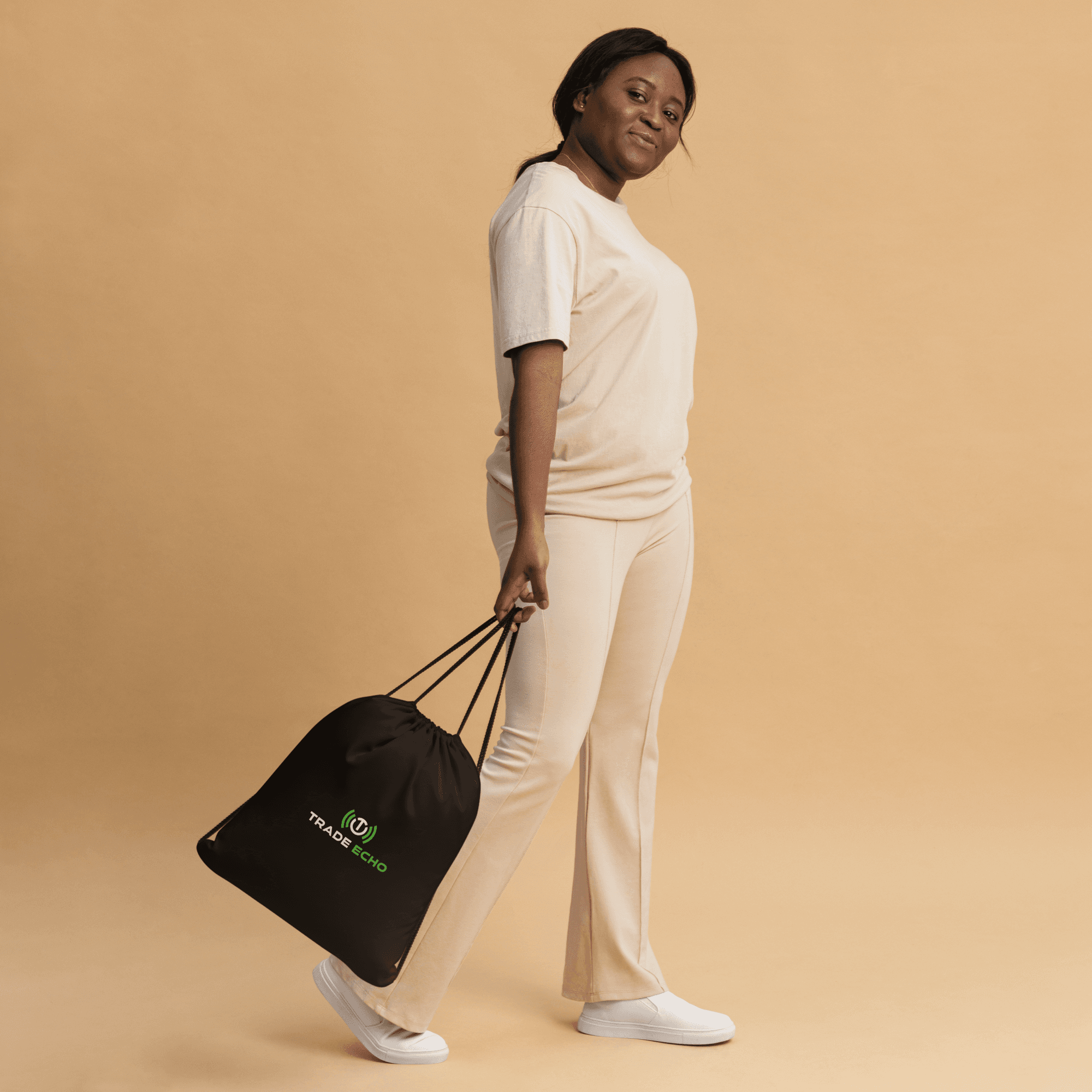 Black Trade Echo drawstring bag carried by its cords at the side, showing the front logo.